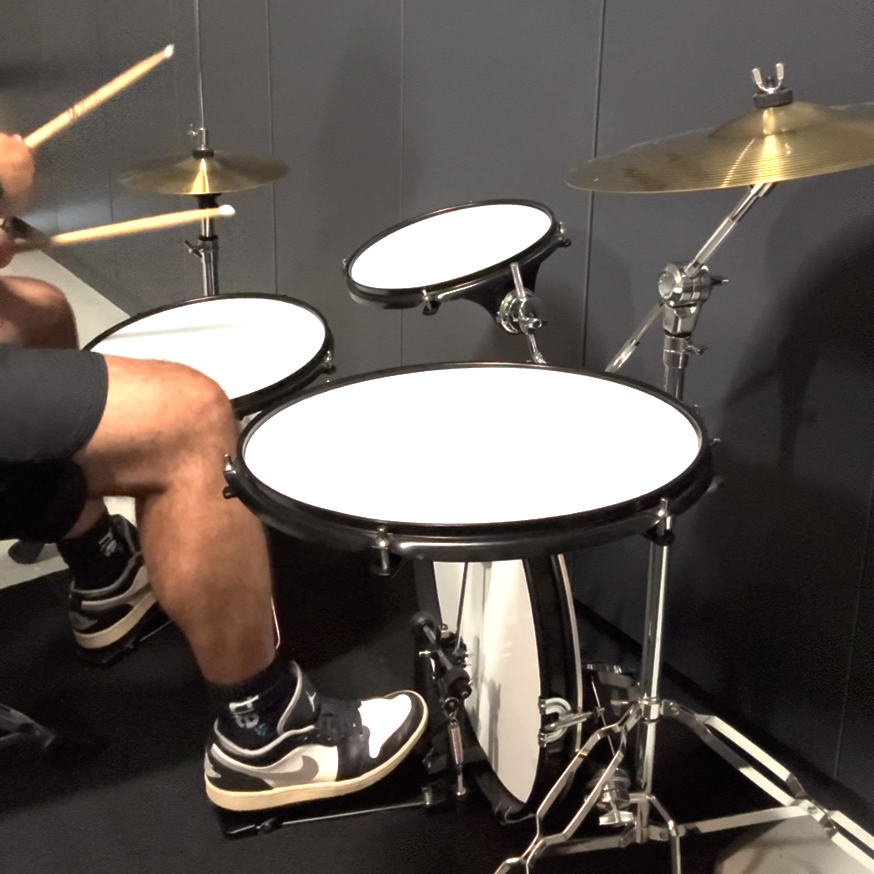 Person playing a drum set in a room with gray walls.